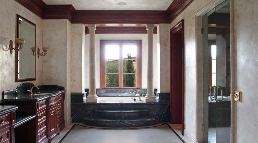 Grand classical primary bath with dark mahogany vanity, black marble tub surround, and ornate column millwork, Corona del Mar