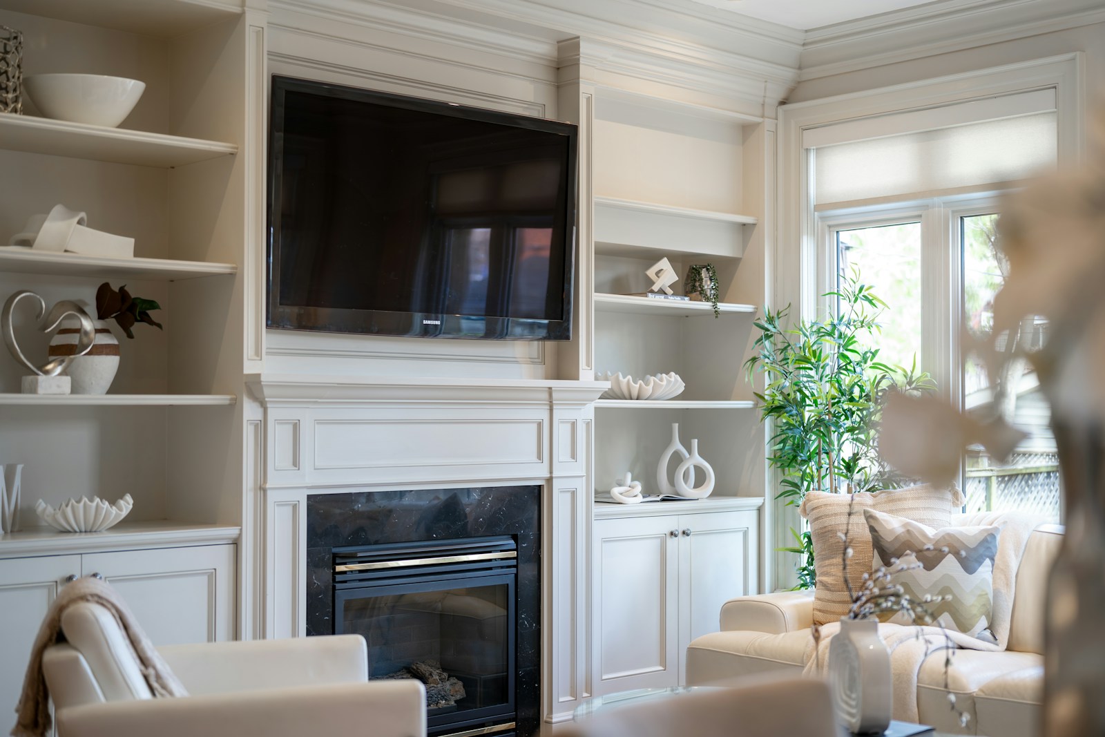White built-in entertainment wall with TV above fireplace and flanking display shelves